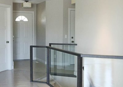 Our results with this staircase are so pretty and open up the space so well. Upstaits hallway with glass railing for stairs and showing white bedroom doors in background.