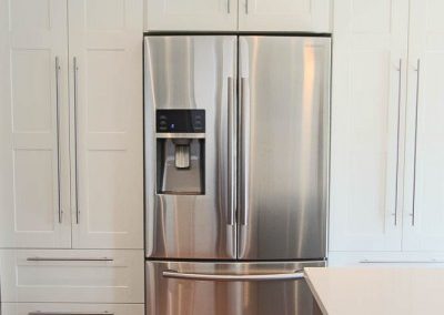 The fridge is surrounded by gorgeous white cabinets and modern silver oversized hardware. Interior Designer and Renovation Services in Calgary, Alberta.